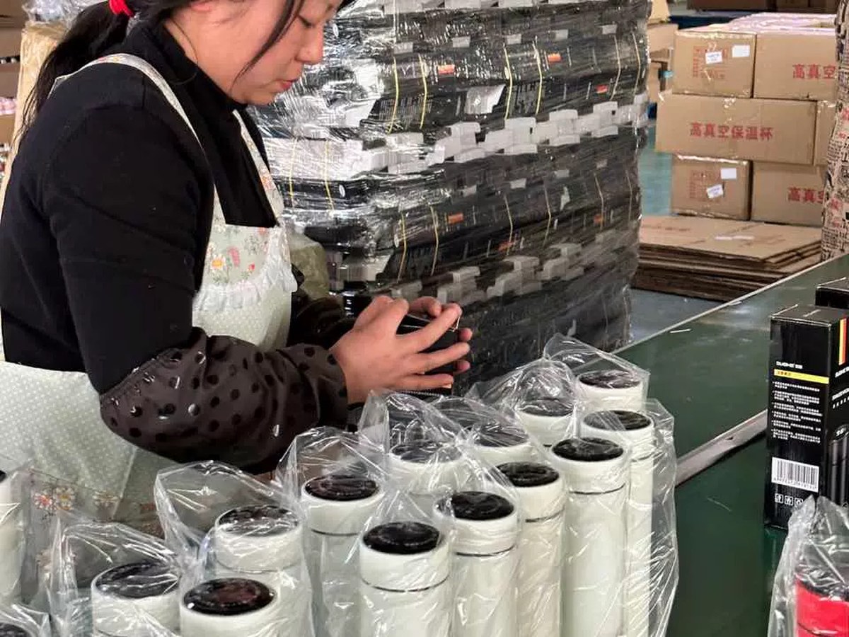 Worker checking finished white drinkware units during batch assembly and packing