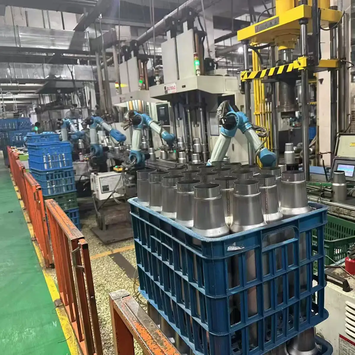 Stainless steel tumbler bodies beside automated forming equipment on a factory production line