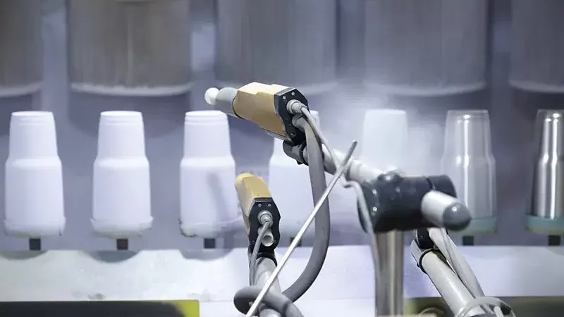 Automated spray guns coating white tumbler bodies on a production line