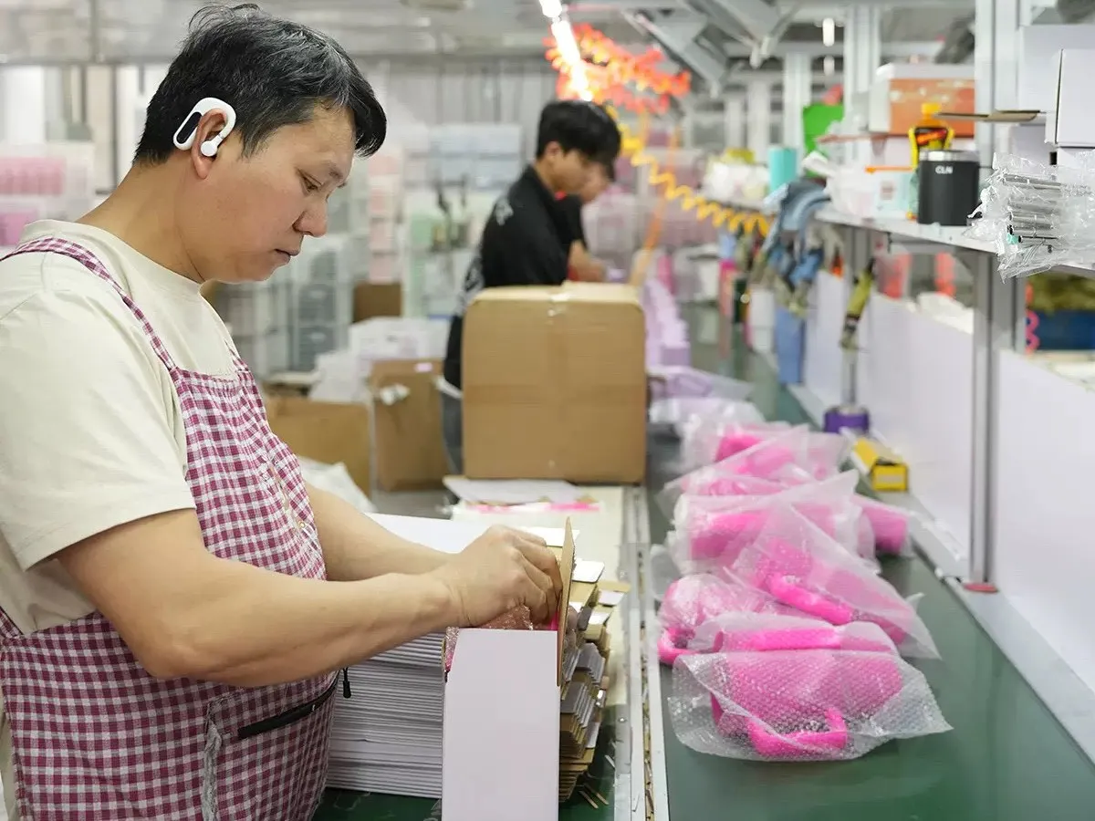 Worker handling packaged colored drinkware components on a factory packing line