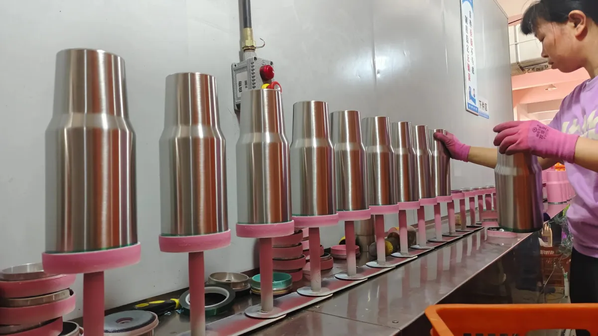 Worker checking stainless steel tumbler bodies before surface coating