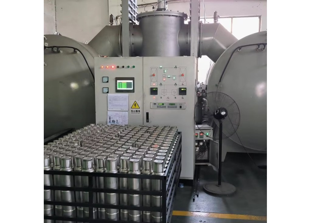 Rows of stainless steel insulated cup bodies staged in front of a twin-chamber vacuum processing system