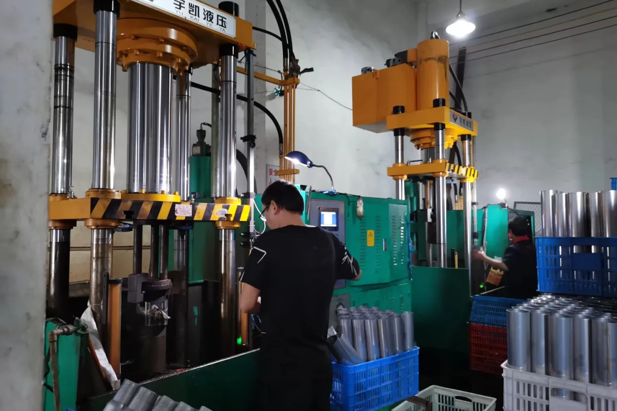Workers operating hydraulic presses beside unfinished stainless steel cup bodies