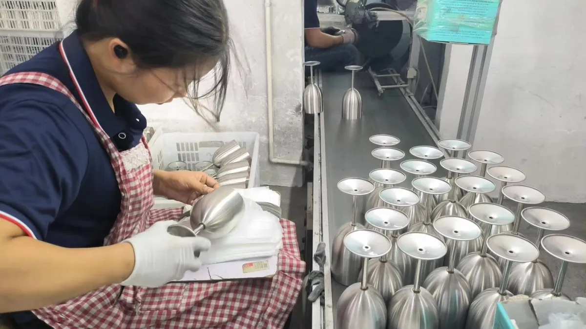 Factory worker handling unfinished stainless steel cup bodies during production inspection