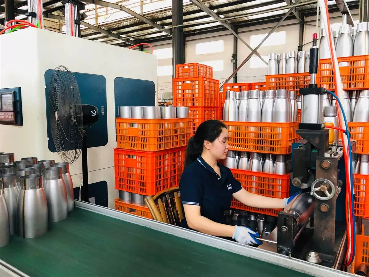 Worker handling stainless steel cup bodies at a drinkware production station