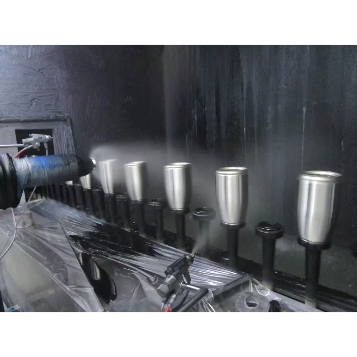 Metal tumbler bodies mounted on rotating fixtures at a factory coating station
