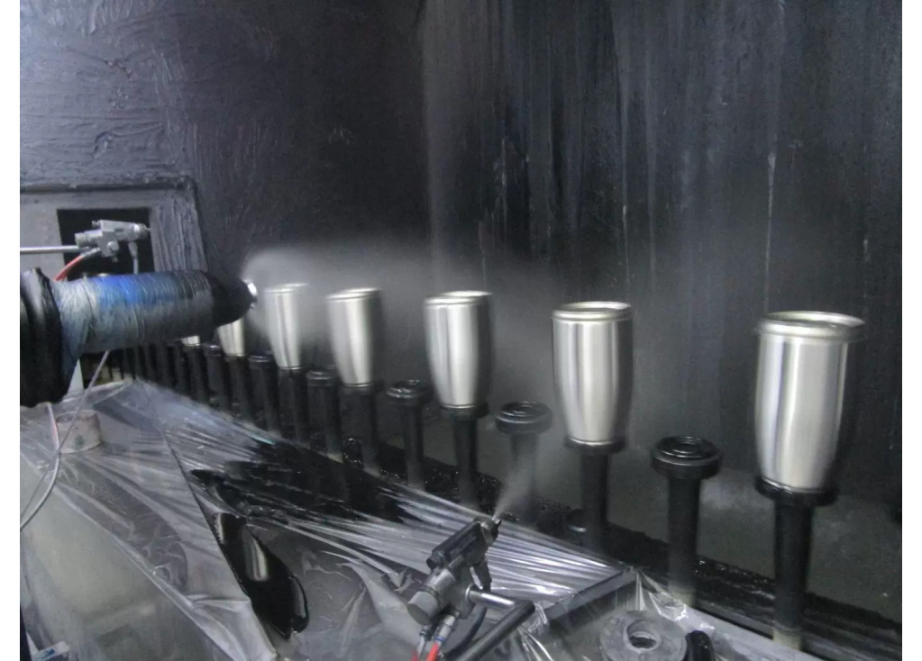 Metal tumbler bodies mounted on rotating fixtures at a factory coating station