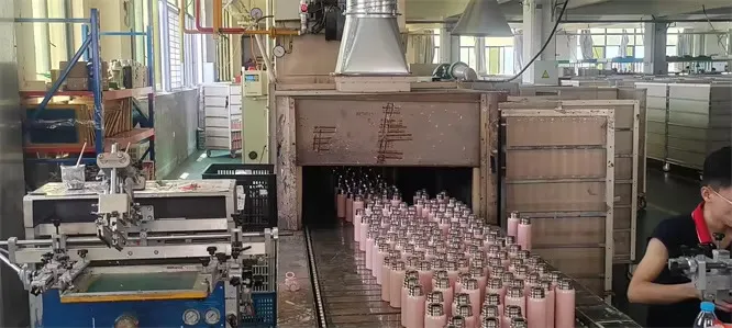 Rows of pink coated tumblers leaving a tunnel-style factory heating line