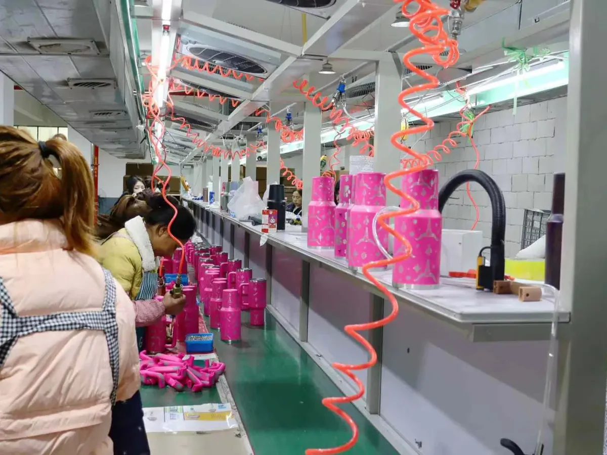 Workers handling bright pink drinkware components at a factory workstation