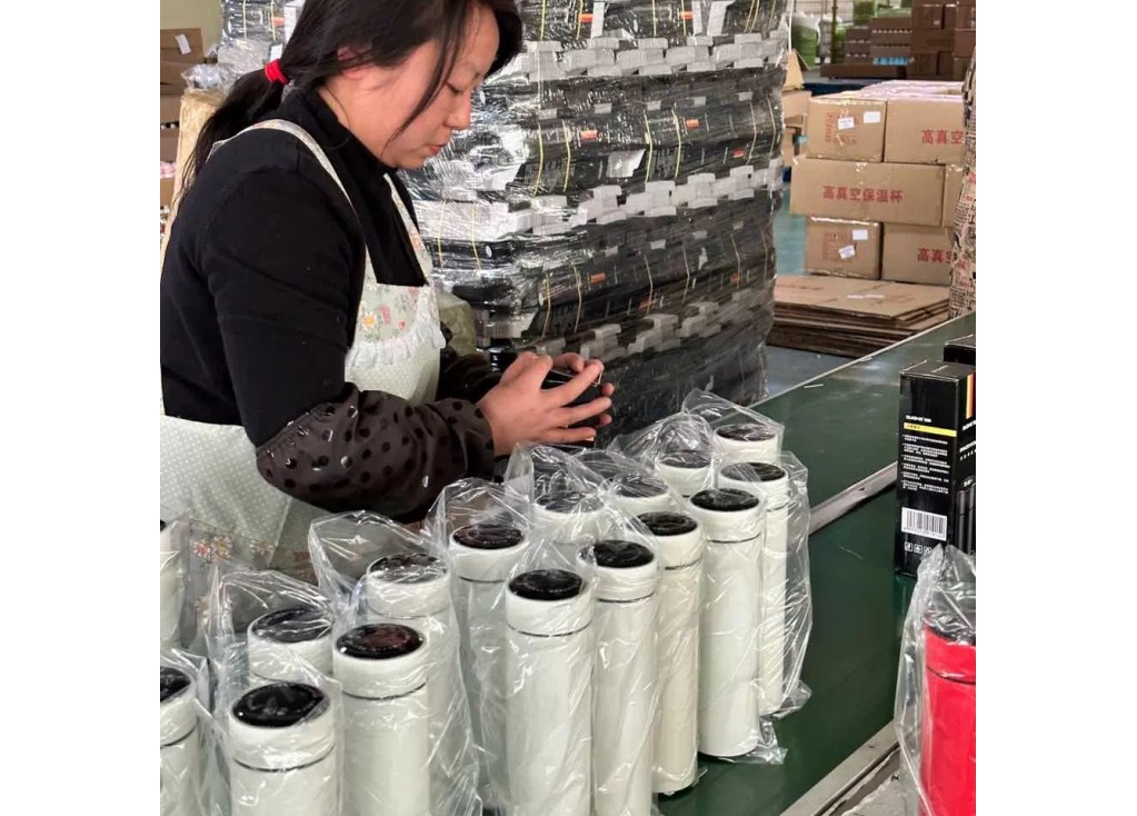 Worker checking a lid component beside finished insulated bottles before packing