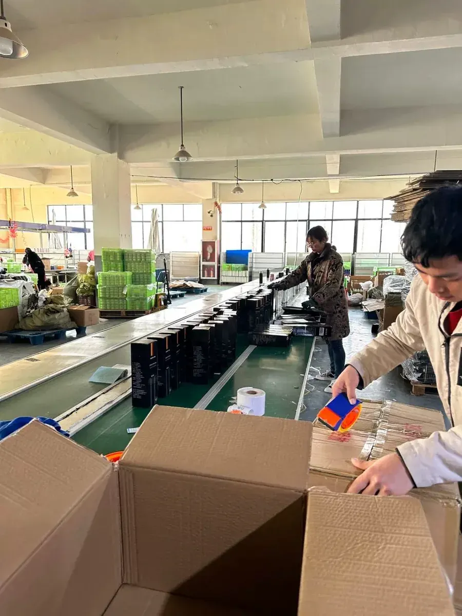Worker using a tape dispenser beside open master cartons on a drinkware packing line
