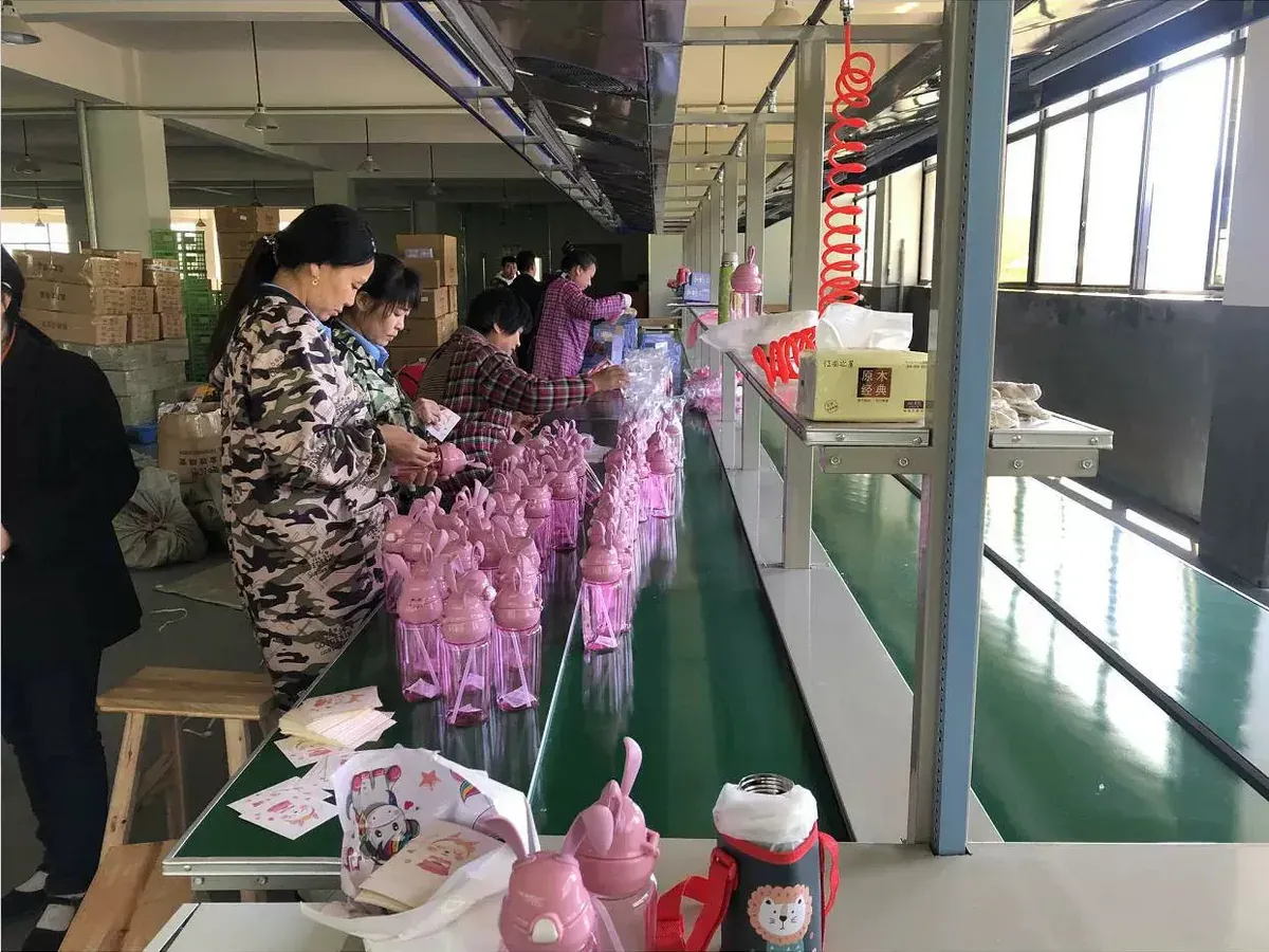 Workers handling pink custom drinkware units on a production line