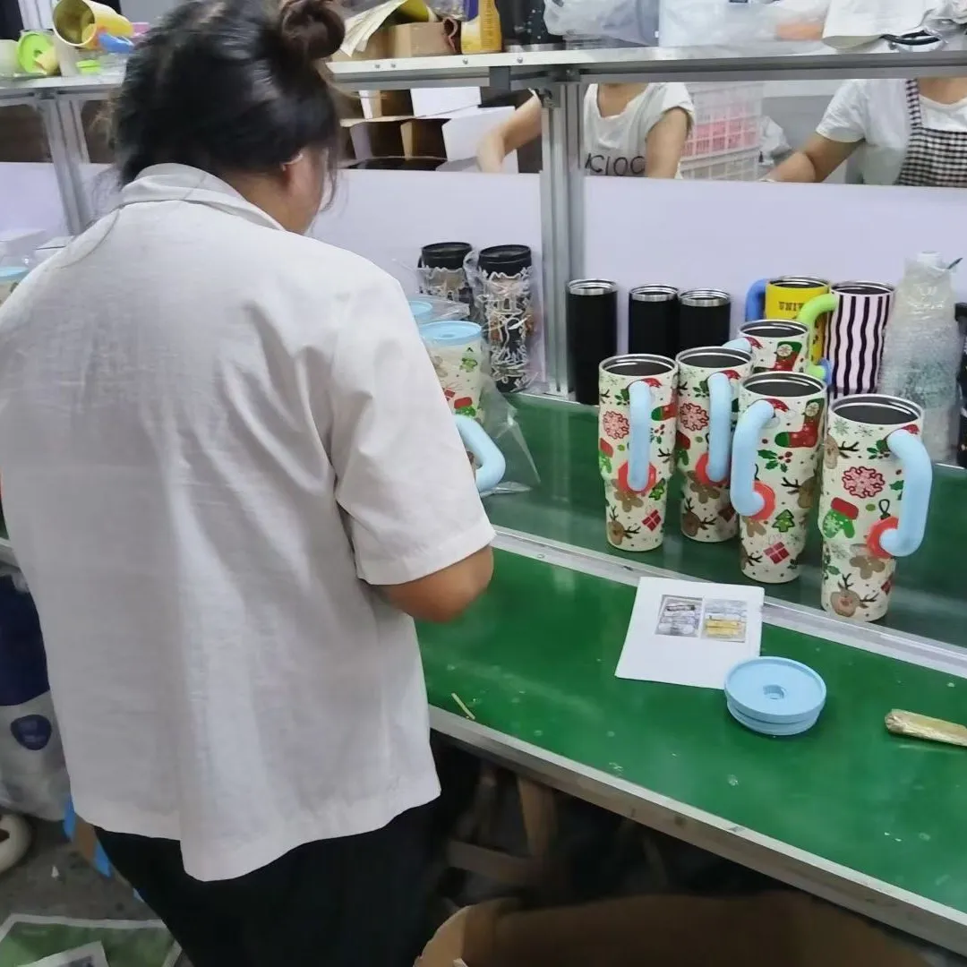 Worker visually inspecting printed tumblers on a factory conveyor
