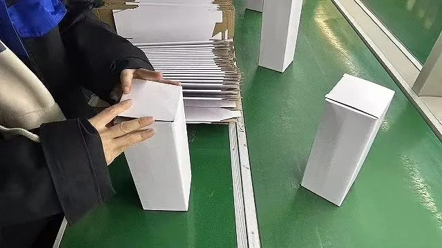 Worker assembling individual white product boxes on a packing line