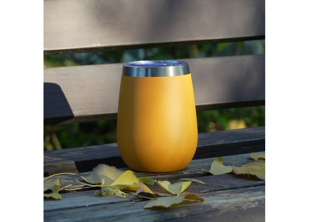 Yellow insulated tumbler on wooden bench with leaves.
