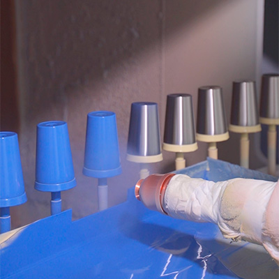 Spray gun applying a blue coating to metal cup bodies